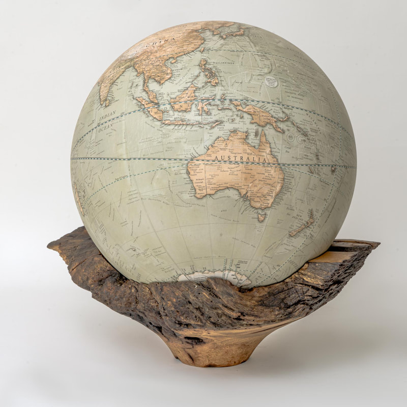 A large contemporary globe sitting in a hollowed wooden bowl, spinning on bearings so it can be spun 360 degrees