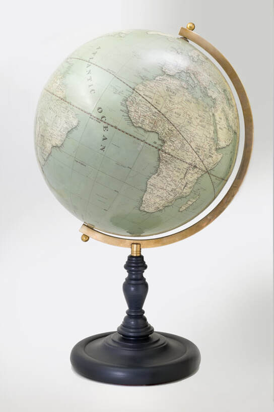 large green globe sideways on, old vintage looking globe but up tom date, with an aged brass arm sitting on top of a turned wooden base