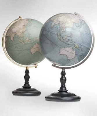 two globes with up to date cartography. One green and one blue, both with a matt black base. One has a brass arm, the other a brushed steel one.